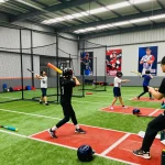 Young athletes training at hitclub indoor baseball facility, practicing swings with coaches.